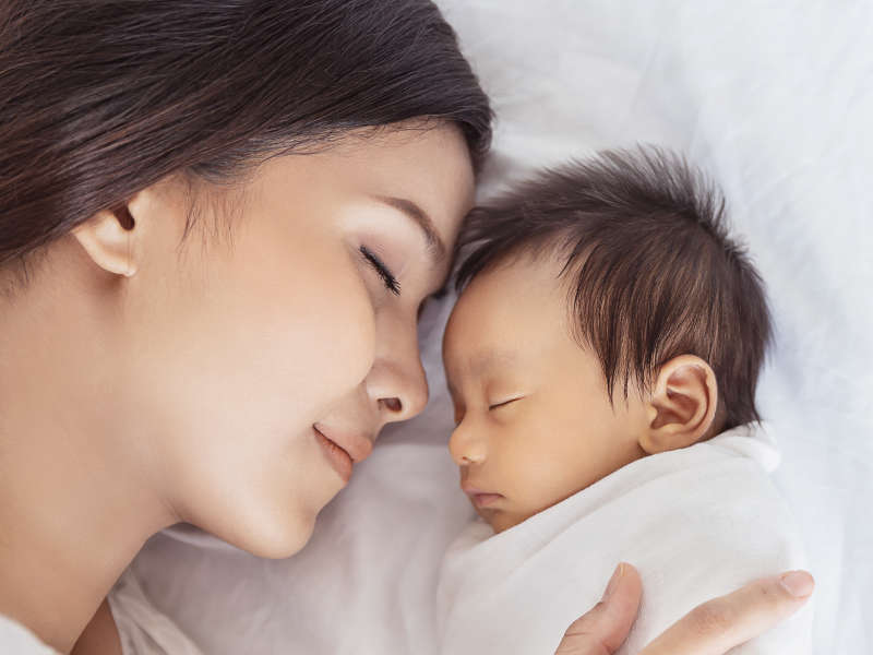Close up portrait of beautiful young Asian mother with healthy newborn baby sleeping in bed